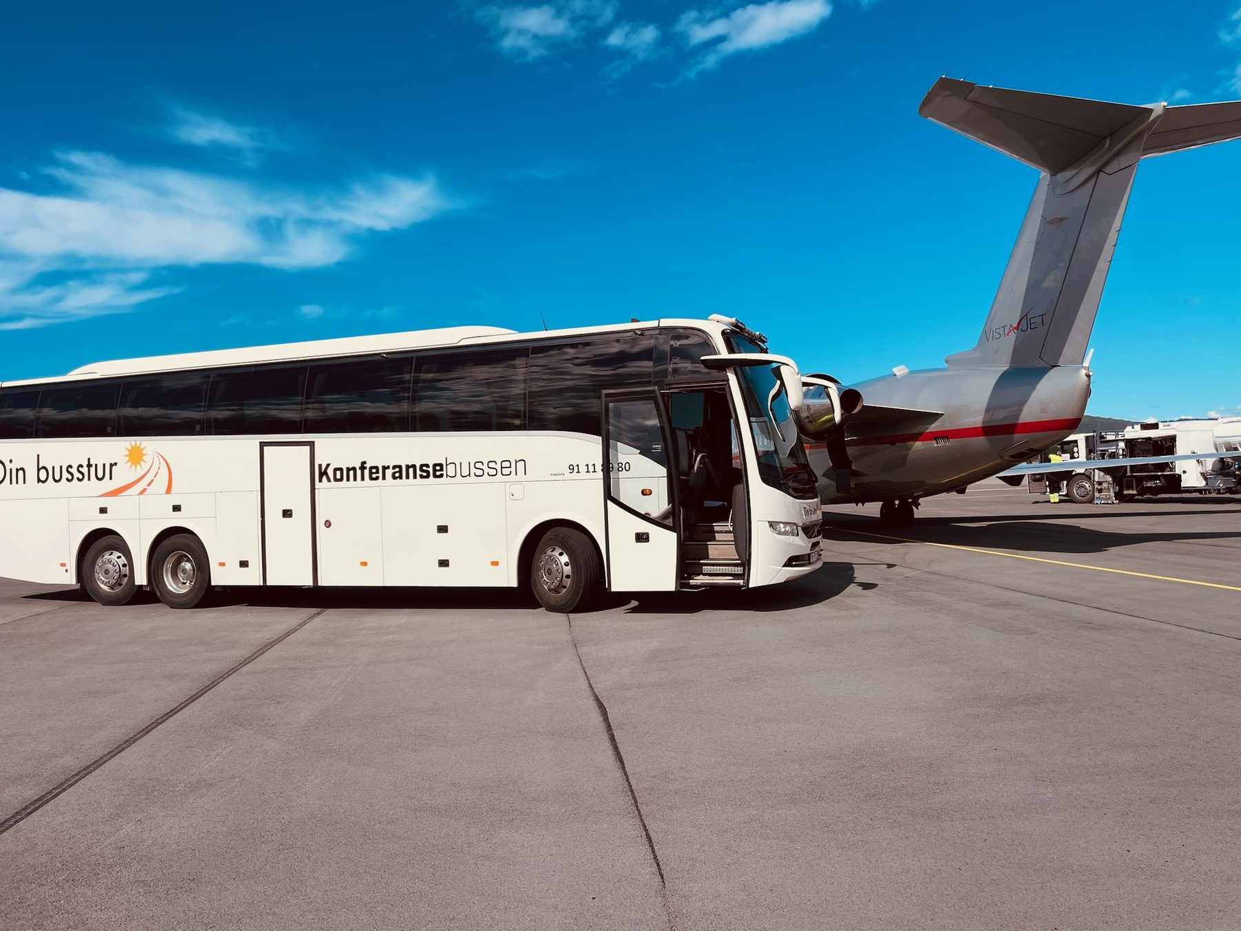 Konferansebussen parkert ved et privatfly på flyplassen, med åpen dør og blå himmel